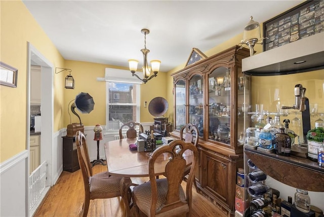 dining area with a wainscoted wall, light wood-style flooring, visible vents, and a notable chandelier