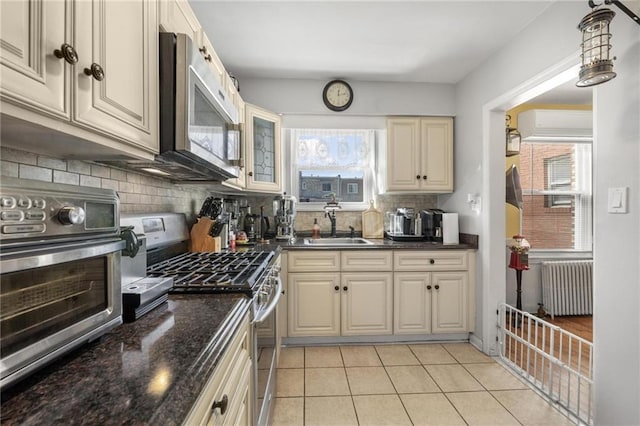 kitchen with stainless steel appliances, a sink, tasteful backsplash, radiator heating unit, and dark stone countertops