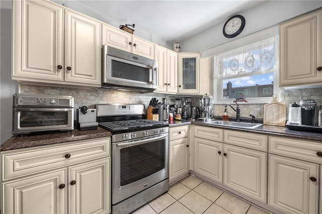 kitchen with light tile patterned floors, stainless steel appliances, backsplash, cream cabinets, and a sink