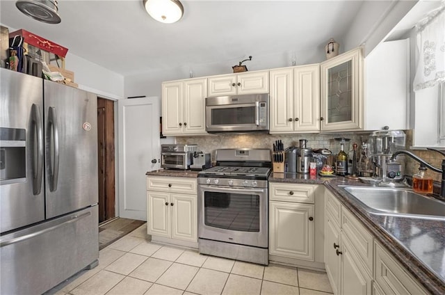 kitchen with glass insert cabinets, a sink, stainless steel appliances, backsplash, and light tile patterned flooring