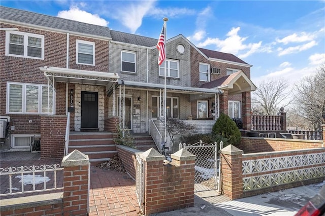 townhome / multi-family property with a fenced front yard, a gate, a shingled roof, and brick siding