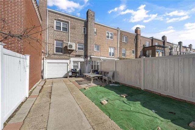 back of house featuring a patio, a fenced backyard, a garage, brick siding, and driveway