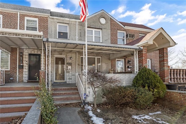 multi unit property featuring a shingled roof, a porch, and brick siding