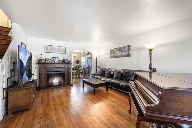 living room with arched walkways, a glass covered fireplace, stairway, and wood finished floors