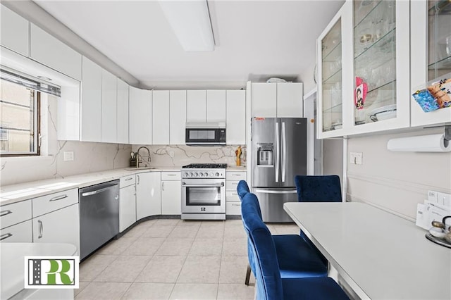 kitchen with glass insert cabinets, light tile patterned flooring, tasteful backsplash, white cabinets, and appliances with stainless steel finishes