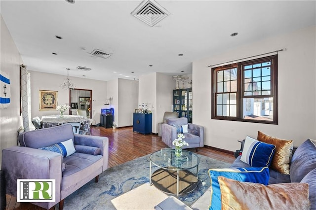 living room with an inviting chandelier, visible vents, baseboards, and wood finished floors