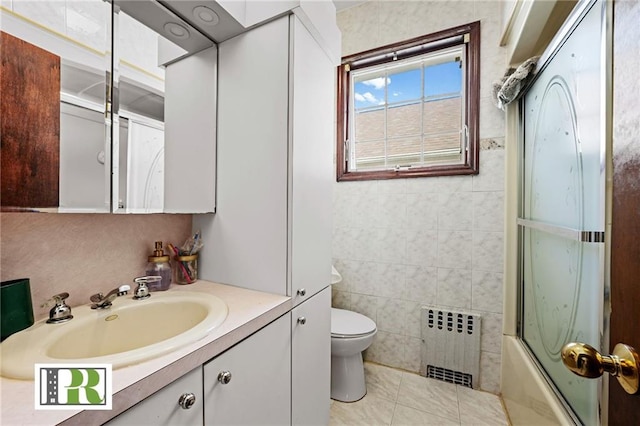 bathroom with radiator, shower / bath combination with glass door, vanity, tile patterned floors, and toilet