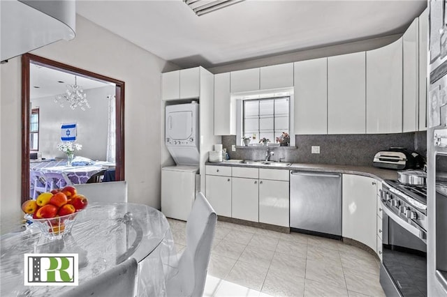 kitchen with stainless steel appliances, a sink, white cabinets, stacked washing maching and dryer, and decorative backsplash