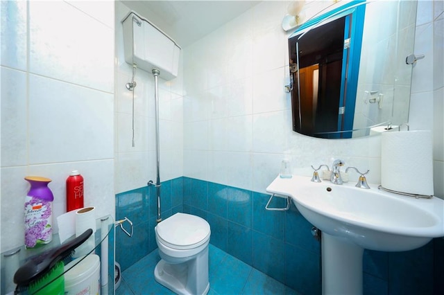 half bath with toilet, a sink, and tile walls