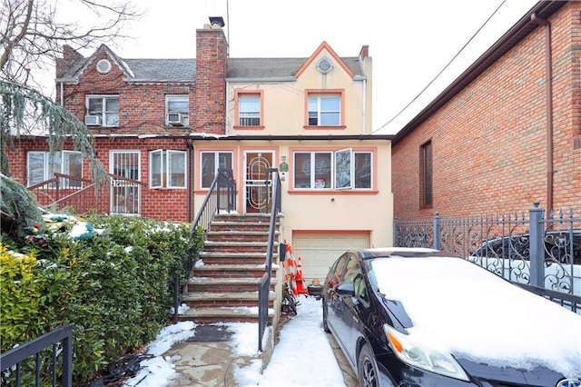 view of front facade featuring a garage, stucco siding, brick siding, driveway, and fence