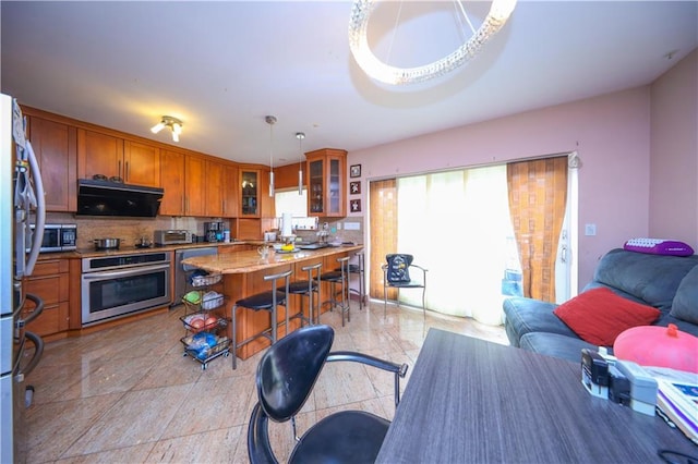 kitchen with brown cabinetry, glass insert cabinets, open floor plan, stainless steel appliances, and pendant lighting