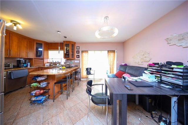 kitchen featuring glass insert cabinets, brown cabinets, a kitchen bar, pendant lighting, and a sink