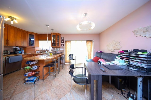 kitchen with brown cabinetry, glass insert cabinets, hanging light fixtures, and a kitchen breakfast bar