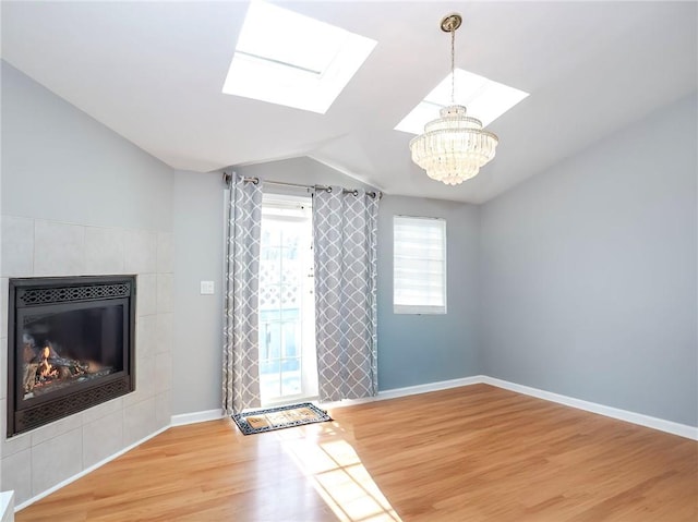 unfurnished living room with vaulted ceiling with skylight, baseboards, a tile fireplace, light wood-type flooring, and a chandelier