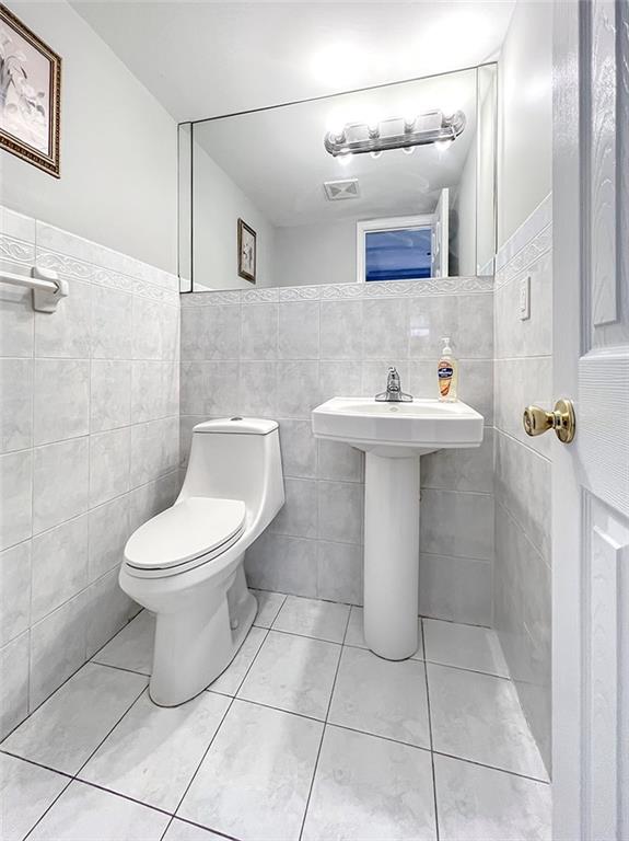 bathroom with toilet, tile patterned floors, visible vents, and tile walls