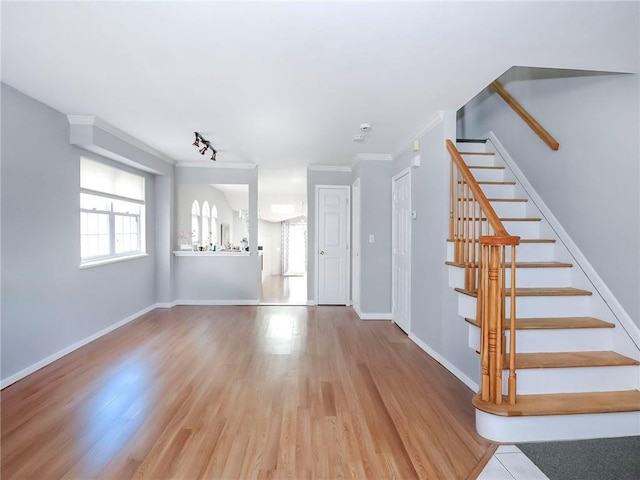 unfurnished living room featuring baseboards, stairway, wood finished floors, crown molding, and track lighting