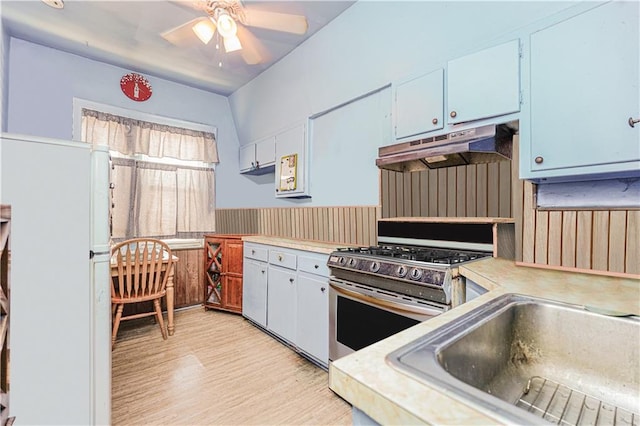 kitchen with stainless steel gas range oven, light wood-style flooring, under cabinet range hood, light countertops, and freestanding refrigerator