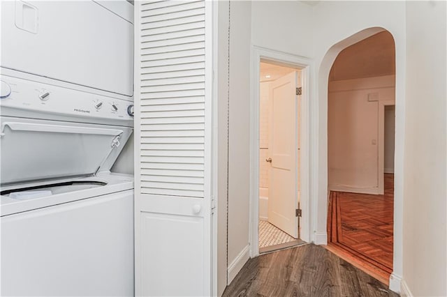 laundry room with laundry area, baseboards, arched walkways, stacked washer / drying machine, and wood finished floors