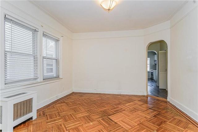 spare room featuring arched walkways, radiator, and baseboards