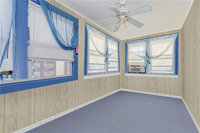 empty room featuring carpet, wooden walls, ceiling fan, and a wealth of natural light