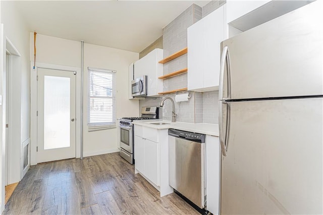 kitchen with white cabinets, stainless steel appliances, light countertops, open shelves, and a sink