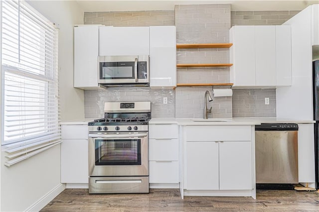 kitchen with appliances with stainless steel finishes, light countertops, a sink, and light wood-style flooring