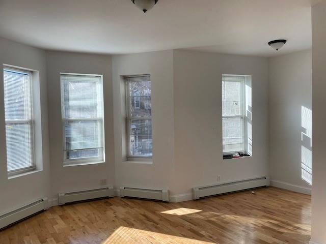unfurnished room with a baseboard radiator, a baseboard heating unit, wood finished floors, and baseboards