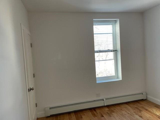 spare room featuring light wood-style floors, a healthy amount of sunlight, a baseboard heating unit, and baseboards