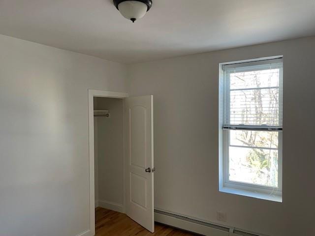 spare room with baseboard heating, wood finished floors, baseboards, and a wealth of natural light