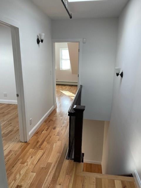 corridor featuring a baseboard radiator, baseboards, an upstairs landing, and light wood-style floors