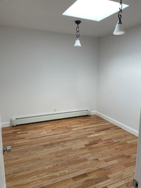 spare room with a baseboard radiator, light wood-type flooring, and baseboards