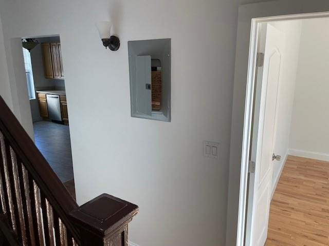 corridor with baseboards, light wood finished floors, and electric panel