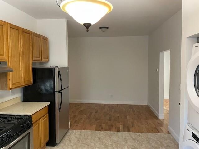 kitchen with light wood-type flooring, stacked washer and dryer, light countertops, under cabinet range hood, and appliances with stainless steel finishes