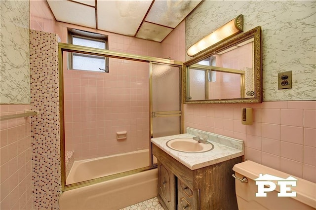 full bathroom with wallpapered walls, bath / shower combo with glass door, tile walls, and a wainscoted wall