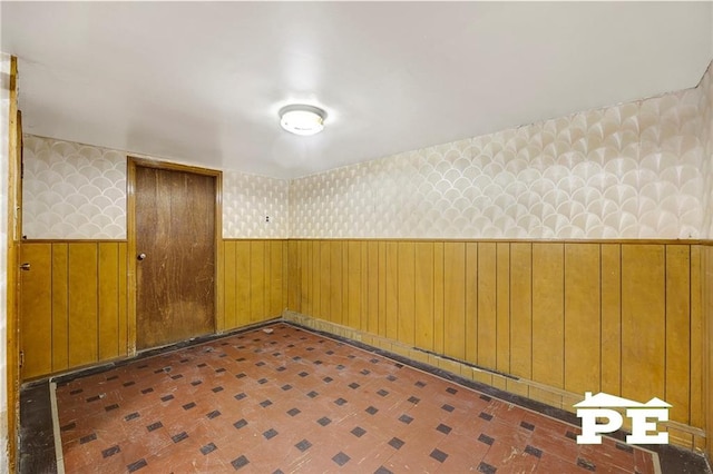 empty room featuring a wainscoted wall, wooden walls, and wallpapered walls