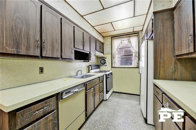 kitchen with dark brown cabinetry, under cabinet range hood, white appliances, a sink, and light countertops