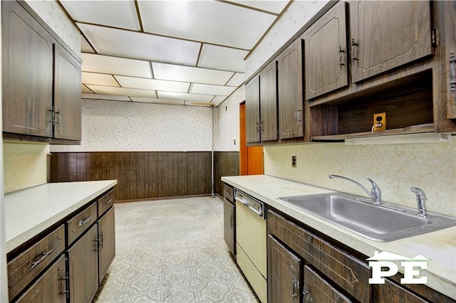 kitchen with a wainscoted wall, dishwashing machine, a sink, and light countertops