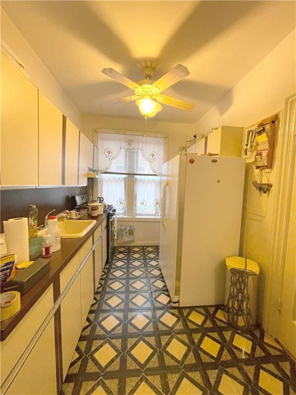 kitchen with stainless steel range oven, white cabinets, a sink, and freestanding refrigerator