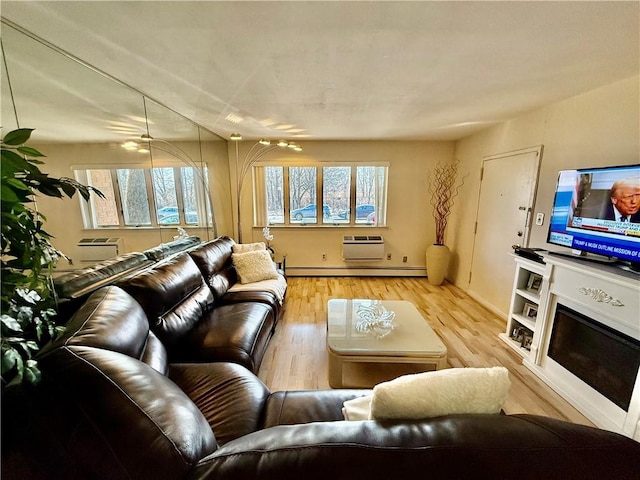 living area featuring light wood-type flooring, an AC wall unit, a glass covered fireplace, and baseboard heating