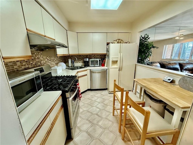 kitchen featuring light floors, backsplash, appliances with stainless steel finishes, a sink, and under cabinet range hood