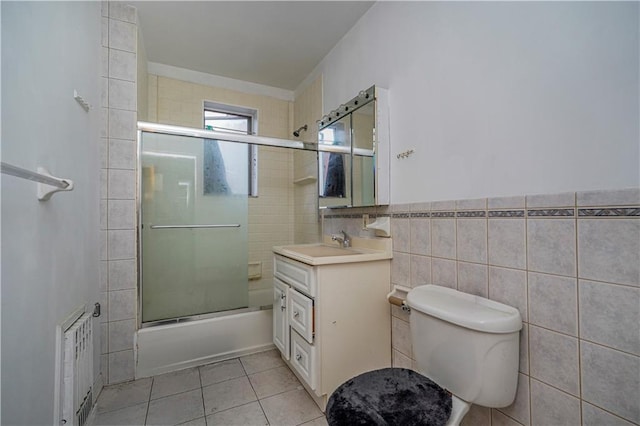 bathroom featuring tile walls, bath / shower combo with glass door, toilet, vanity, and tile patterned floors