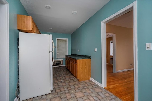 kitchen with baseboards, freestanding refrigerator, heating unit, brown cabinetry, and dark countertops