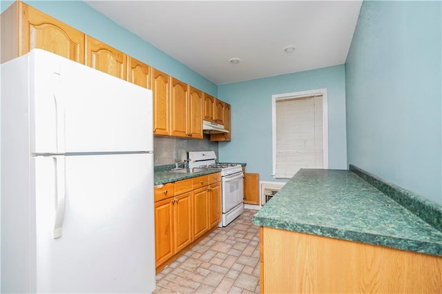 kitchen with dark countertops, white appliances, under cabinet range hood, and backsplash