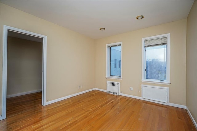 empty room with baseboards, radiator heating unit, and light wood-style floors