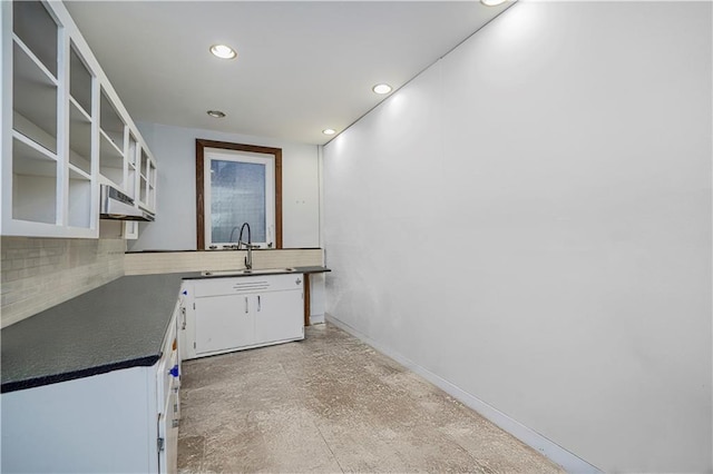 kitchen featuring a sink, white cabinets, backsplash, dark countertops, and glass insert cabinets