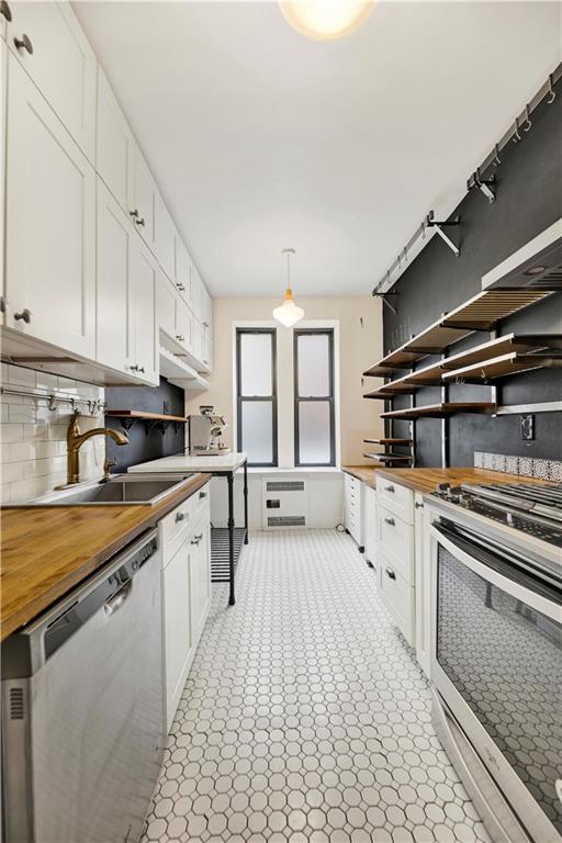 kitchen with a sink, wood counters, white cabinetry, hanging light fixtures, and appliances with stainless steel finishes