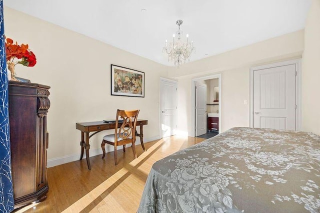 bedroom featuring light wood-type flooring, an inviting chandelier, ensuite bath, and baseboards