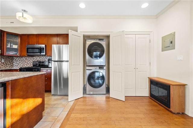 kitchen with crown molding, appliances with stainless steel finishes, stacked washer / dryer, glass insert cabinets, and electric panel