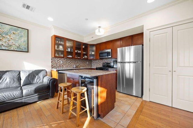 kitchen featuring visible vents, appliances with stainless steel finishes, glass insert cabinets, a kitchen island, and a kitchen breakfast bar