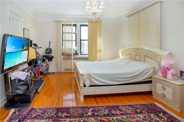 bedroom featuring light wood-style flooring, radiator heating unit, and an inviting chandelier